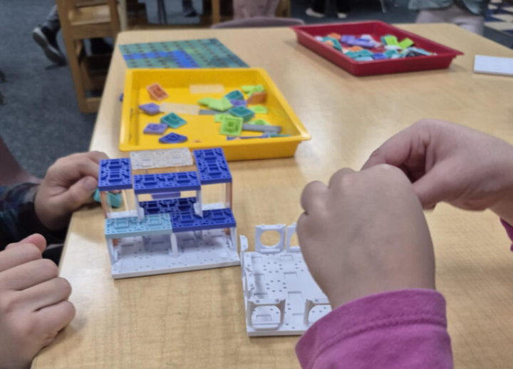Two children's hands work on a building project at a table.