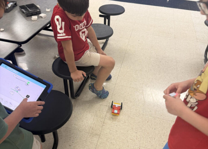 Three children work with an ipad and a robot to code it.