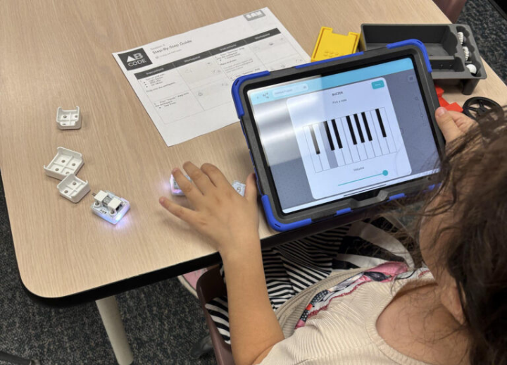 A girl uses a lap top to create early coding work at a table.