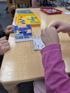 Two children's hands work on a building project at a table.