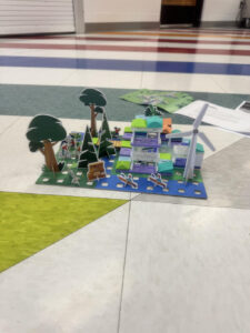 A child-made display of a house and yard landscape sitting on the ground.