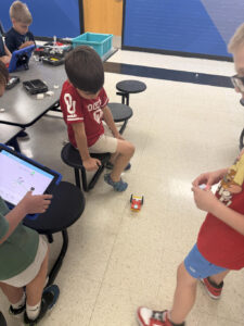 Three children work with an ipad and a robot to code it.