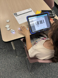 A girl uses a lap top to create early coding work at a table.