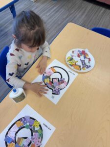 Girl works on letter Q decoration at table.