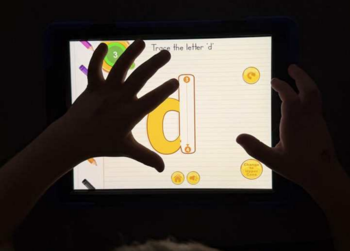 Children's hand using iPad to trace the letter D.